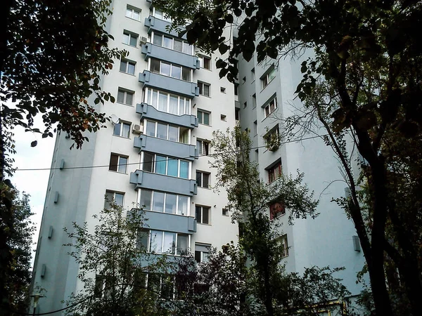 The multi-storey urban panel building of a blue shade with balconies surrounded by trees. Noticeable sky and wire high-voltage lines — Stock Photo, Image