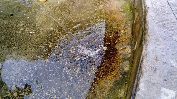 Fuente antigua en el centro de la ciudad. Una fina corriente de agua se vierte en el mismo lugar, que cambió de color a oxidado. Reflejo del cielo en el agua —  Fotos de Stock