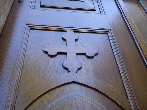 Wooden old church door. Carved wooden cross and varnished, smooth surface, shining in natural light — ストック写真