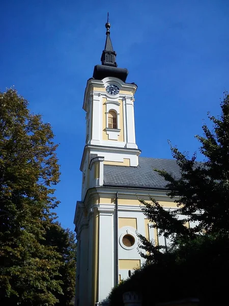 Część kościoła z kopułą i zegarem pod spodem. Świątynia malowana jest w kolorze białym - żółtym, kopuła i iglica - czarnym. Wczesna jesień z błękitnym niebem — Zdjęcie stockowe
