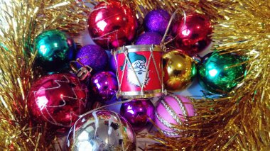 Noel ağacı için parlak cam oyuncaklar altın süslemelerin yanında yatar. Ortada içinde Noel Baba resmi olan küçük bir plastik varil var.