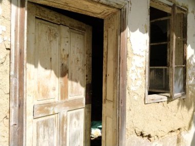 Eski pencereleri ve çökmekte olan kırsal bir evin kapısı olan bir duvar. Kentleşme ve anavatanın unutulması kavramı. Terk edilmiş bir ev. Pencerelerde kırık cam ve düşen alçı.