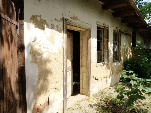 Parede com janelas antigas e uma porta em uma casa rural em colapso. O conceito de urbanização e esquecimento da pátria. Casa abandonada. Vidro quebrado nas janelas e gesso caindo — Fotografia de Stock