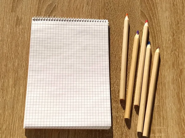 空の白いページが木製のテーブルの上に横たわっている空白のメモ帳を開きます テーブルの上に開いているノートと5色の鉛筆 — ストック写真