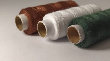 Bobinler ve iplikler farklı renklerde - kahverengi, beyaz ve yeşil. Yakın plan. Sol tarafta doğal ışık var. İplik derileri. Dikiş malzemeleri. Tekstil üretimi