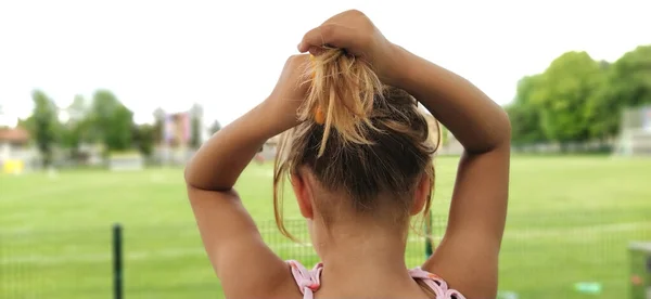 young pretty woman tied her hair. A girl is photographed from the back against the backdrop of a soccer field. The formation of the tail of the hair. Serbia, Belgrade. Banner.