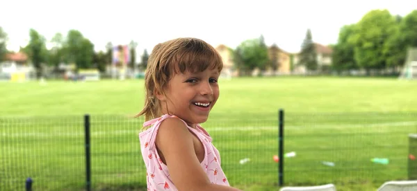 Młoda Piękna Opalona Dziewczyna Odwraca Się Uśmiecha Dziecko Tle Boiska — Zdjęcie stockowe
