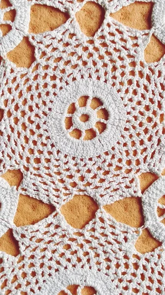 Handgehäkelte weiße Spitze. Runde Serviette für Tisch oder Kommode. Ornament im traditionellen rustikalen Stil. Ordentlich gehäkelt oder gestrickt. Weiße Fäden aus Baumwolle. Orange Hintergrund — Stockfoto