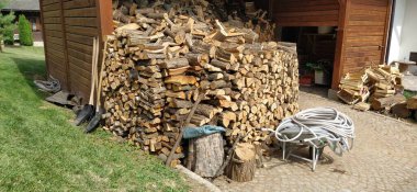 Ahırda odun var. Malzeme odasının etrafında odun, kauçuk hortumlar, ev aletleri var. Etno tarzında bir restoran arka bahçesi. Ahşap mimari.