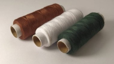 Bobinler ve iplikler farklı renklerde - kahverengi, beyaz ve yeşil. Yakın plan. Sol tarafta doğal ışık var. İplik derileri. Dikiş malzemeleri..