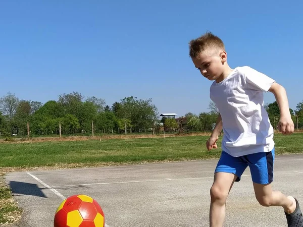A boy runs after a basketball ball. The child plays with a ball on the playground. Free space for text. Blue sky in the background. Child with blond hair.