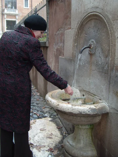 ローマ イタリア 2019年12月10日 黒いコートを着た中年の女性が噴水で手を洗う 記念碑の泉からは水が流れている 古代の水路 — ストック写真