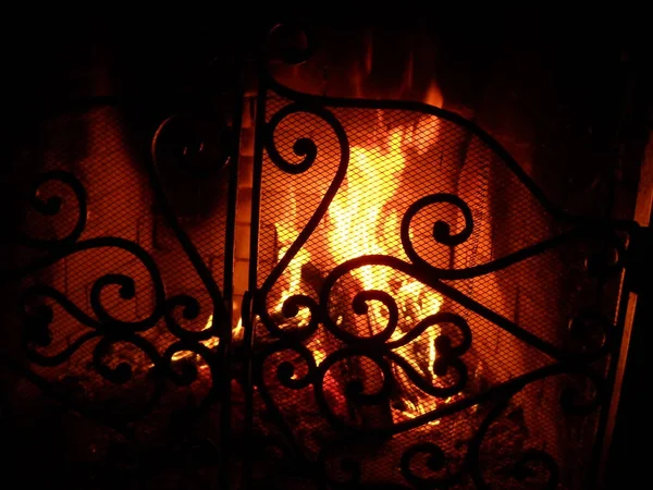 Φωτιά στο τζάκι πίσω από μια όμορφη σιδερένια σχάρα με μπούκλες. Καίγεται φωτιά στο τζάκι. Νύχτα και φωτιά στο σκοτάδι — Φωτογραφία Αρχείου