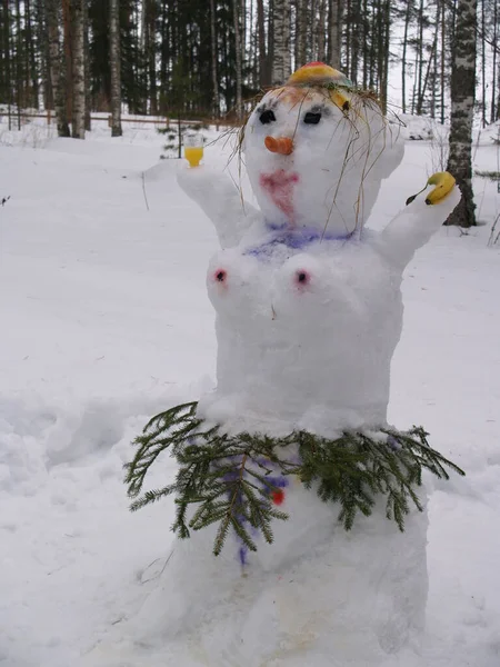 Een sneeuwvrouw gemaakt van sneeuw. Ze heeft een banaan in de ene hand, en een wodka glas in de andere. Het haar is gemaakt van stro, de snowmans rok is gemaakt van sparren takken. Het gezicht en de details op de borst — Stockfoto