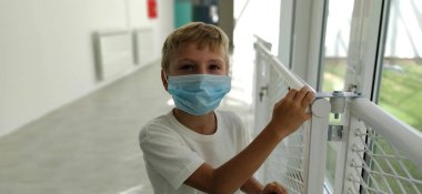 Okul koridorundaki maskeli çocuk. Yeni modern okul ya da tadilattan sonra okul. 8 yaşında sarı saçlı ve yüzünde mavi cerrahi koruyucu maske olan bir çocuk. Coronavirus COVID 19.