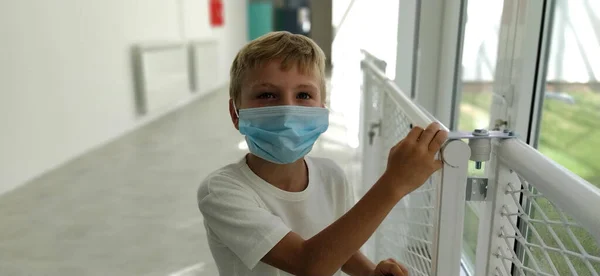 Masked boy in the school hallway. New modern school or school after renovation. A child of 8 years old with blond hair and a blue surgical protective mask on his face. Coronavirus COVID 19.