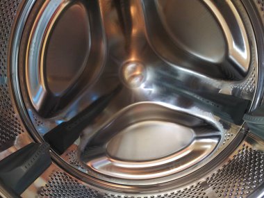 Çamaşır makinesinin varili içeriden. Delikleri ve çıkıntıları olan parlak metal bir tank. Paslanmaz çelikten yapılmış delikli paslanmaz çelik yüzey. Bir çamaşır makinesinin iç görünümü.