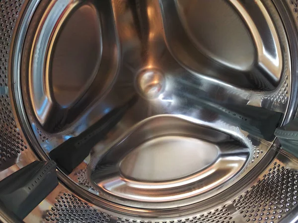 Çamaşır makinesinin varili içeriden. Delikleri ve çıkıntıları olan parlak metal bir tank. Paslanmaz çelikten yapılmış delikli paslanmaz çelik yüzey. Bir çamaşır makinesinin iç görünümü.