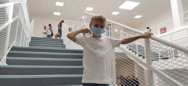 Sremska Mitrovica, Sırbistan, 1 Eylül 2020. Beyaz gömlekli ve maskeli bir çocuk merdivenlerde poz veriyor. 7 yaşında bir çocuk tırabzana tutunuyor. Modern okul, klinik ya da beyaz duvarlı hastane.