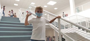 Sremska Mitrovica, Sırbistan, 1 Eylül 2020. Beyaz gömlekli ve maskeli bir çocuk merdivenlerde poz veriyor. 7 yaşında bir çocuk tırabzana tutunuyor. Modern okul, klinik ya da beyaz duvarlı hastane.