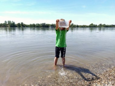 Plajda plastik ambalajla oynayan bir kız. Sudaki bebek. Ekoloji ve çevre koruma kavramı. Oyun için fikir. Kıyıdaki çocuklar. Sırbistan, Sava Nehri