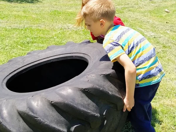 Çocuklar oynar ve lastikleri kaldırır. Çocuk oyununda araba parçaları ve aksesuarlar. Bir erkek ve bir kız 6 ve 7 yaşlarında çimlerin üzerinde güç egzersizleri yapıyorlar. Sarı saçlı insanlar..