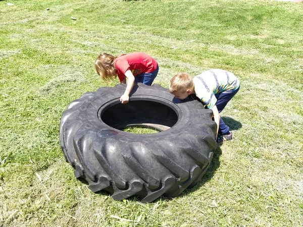 Sremska Mitrovica, Sırbistan, 20 Mayıs 2020. Çocuklar oynar ve lastikleri kaldırır. Çocuk oyununda araba parçaları ve aksesuarlar. Bir erkek ve bir kız 6 ve 7 yaşlarında çimlerin üzerinde güç egzersizleri yapıyorlar..