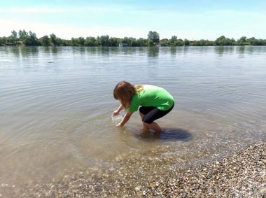 7-8 yaşlarında, İsviçre Alplerinde yürüyüş yapan, nehir kenarında dinlenen, spor giysileri, spor ayakkabıları ve sırt çantası giyen,