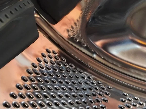 The drum of the washing machine from the inside. Shiny metal tank with holes and bulges. Stainless steel surface with holes, made of stainless steel sheet. Interior view of a Washing machine.