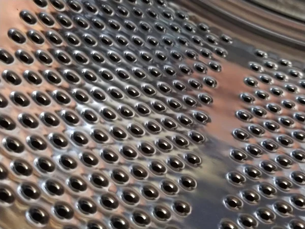 The drum of the washing machine from the inside. Shiny metal tank with holes and bulges. Stainless steel surface with holes, made of stainless steel sheet. Interior view of a Washing machine.