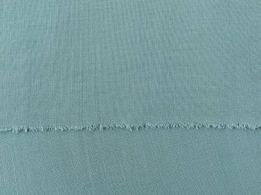 Yünlü kumaşın yeşil ya da mavi renkte yırtılmış kenarı. Bir tekstil parçasının kenarındaki gevşek iplikler. Yakın plan. Örülmüş arka plan. Sakin yeşil pastel rengi.