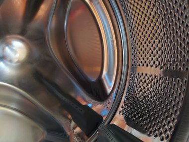 Çamaşır makinesinin varili içeriden. Delikleri ve çıkıntıları olan parlak metal bir tank. Paslanmaz çelik yüzey