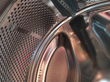 Çamaşır makinesinin varili içeriden. Delikleri ve çıkıntıları olan parlak metal bir tank. Paslanmaz çelikten yapılmış delikli paslanmaz çelik yüzey. Bir çamaşır makinesinin iç görünümü