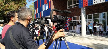 Sremska Mitrovica, Sırbistan, 1 Eylül 2020. Erkek, kameralı bir TV muhabiri. 1 Eylül 'den canlı yayın. Yeni bir okulun açılışı. Kameralar ve fotoğraf makineleri nesnelere yöneliktir.