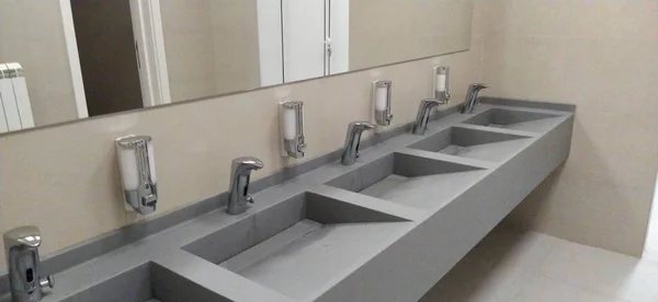 新しい公衆トイレで手を洗うためのシンク 容器に液体石鹸 壁に鏡 明るい色のインテリア 洗面器と蛇口付きのバスルームのインテリア — ストック写真