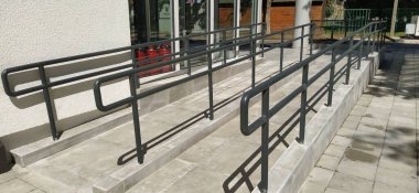 Binanın girişinin yanındaki engelli rampaları. Modern standartlara göre donatılmış yeni okul. Erişilebilir çevre. Engelliler için aletler. Metal parmaklıklar ve yan yamaçlar.