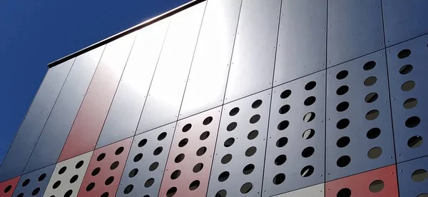 Facade of a modern building. Red, blue and white slabs or metal profiles with decorative holes. Technological solutions in the exterior. Building supporting structures under decorative elements.