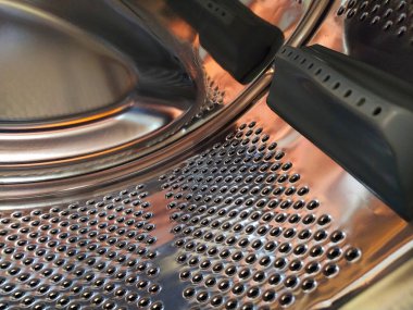 Çamaşır makinesinin varili içeriden. Delikleri ve çıkıntıları olan parlak metal bir tank. Paslanmaz çelikten yapılmış delikli paslanmaz çelik yüzey. Bir çamaşır makinesinin iç görünümü.