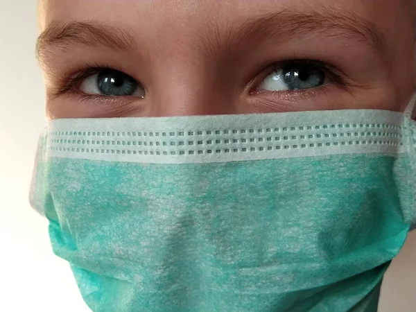 Masked child. The face of a 7-year-old boy in a protective surgical mask close-up. Schoolboy with blond hair and blue-gray eyes on white background.