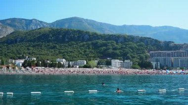 Karadağ 'ın Canj kenti 08.10.2025: plaj Adriyatik Denizi' nin güzel bir manzarası ve kıyıya vuran hafif dalgalar sunuyor. Güneş banyosu yapanlar sıcacık güneşin tadını çıkarırken, etrafları yemyeşil dağlarla çevrili tekneler yüzüyor..