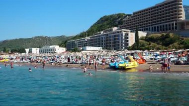 Canj, Karadağ 08.10.2025: Ziyaretçiler Barda neşeli bir plaj günü geçiriyor. İnsanlar kumlu sahilde dinlenirken ve güzel Adriyatik Denizi 'nin ortasındaki su aktivitelerine katılırken güneş ışıldıyor..