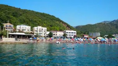 Canj, Karadağ 08.10.2025: Güneş banyosu yapanlar, Adriyatik Denizi 'nin canlı şemsiyeleri ve dingin dalgalarıyla çevrili plajda dinleniyorlar. Açık mavi sular yüzme meraklılarını mükemmel bir yaz gününün tadını çıkarmaya davet eder..