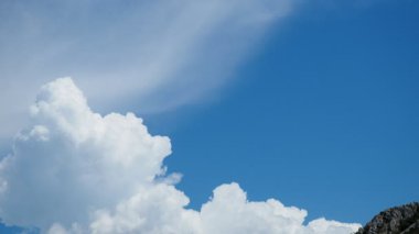 Yumuşak, kabarık bulutlar canlı mavi gökyüzünde tembelce sürüklenerek doğal güzellikleri resmediyor. Parlak güneş ışığı sahnenin sakin atmosferini güçlendirir. Yavaş çekim.