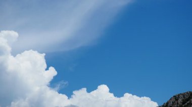 Pofuduk beyaz bulutlarla dolu parlak mavi gökyüzü sakin bir atmosfer yaratır. Aşağıdaki manzara, doğanın güzelliğini artırmak için yuvarlanan tepeleri ve temiz havayı içeriyor. Yavaş çekim