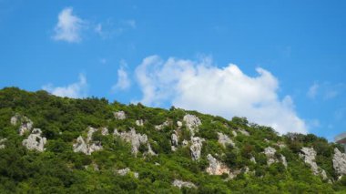 Canlı mavi bir gökyüzünün altında, engebeli uçurumlar görkemli bir şekilde yükseliyor, yeşil yapraklar ve bulut parçalarıyla çevrili. Bu huzurlu yerde doğa güzelliği cezbediyor. Karadağ 'ın Doğası.