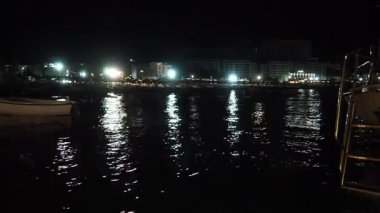 Canj, Chanj, Karadağ, 08.05.2025: Gece Adriyatik Denizi boyunca sakin dalgalar yavaşça sahile vururken, yakındaki tesislerin ışıkları su yüzeyinde parıldıyor.