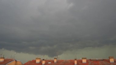 Karanlık fırtına bulutları kaygı verici bir şekilde tepemizde belirdi. Öğleden sonra yaklaşırken sakin bir muhitte çatıların üzerine gölgeler serdi. Yaklaşan yağmur hissi havayı dolduruyor.
