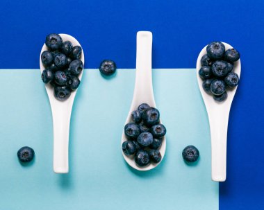 Mavi arka plan üzerinde beyaz kaşık üzerinde modern yaban mersini