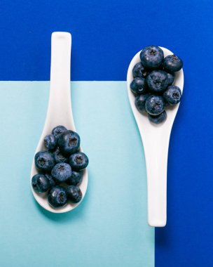 Mavi arka plan üzerinde beyaz kaşık üzerinde modern yaban mersini