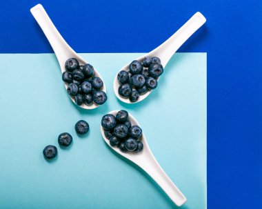 Mavi arka plan üzerinde beyaz kaşık üzerinde modern yaban mersini